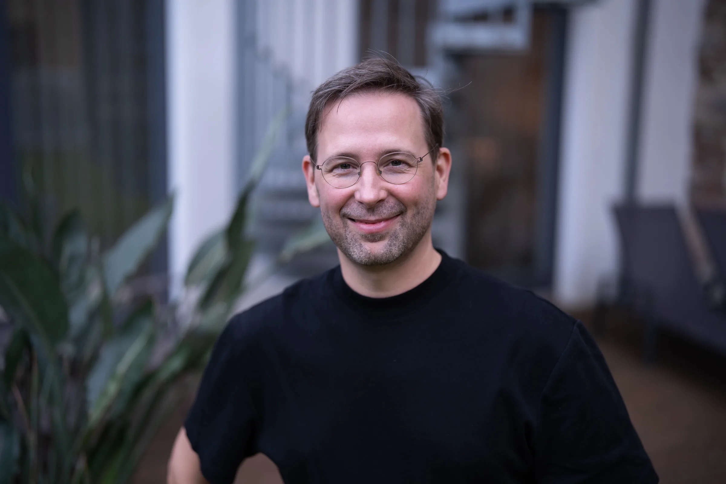 Philipp Neuberger im schwarzen T-Shirt, freundlich lächelnd, in einem Innenhof