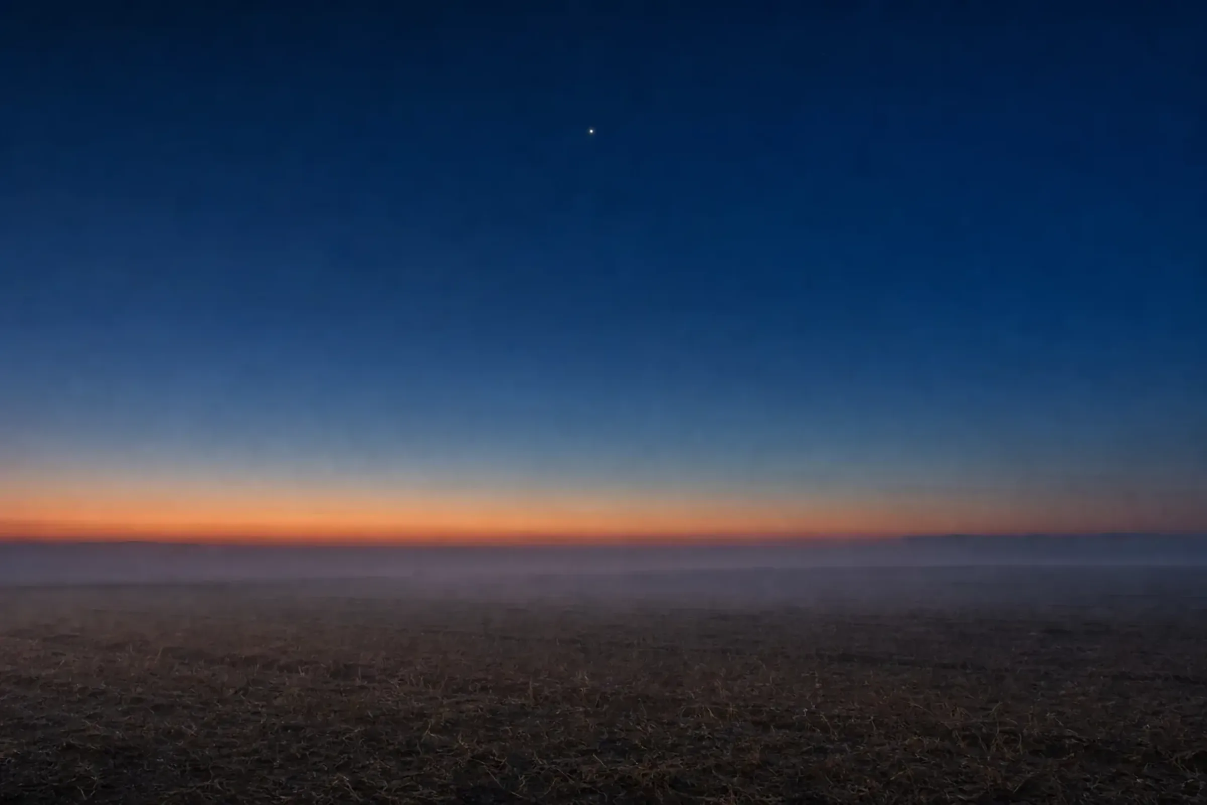 Weite, stille Ebene in der blauen Stunde, hoch darüber ein einzelner heller Stern